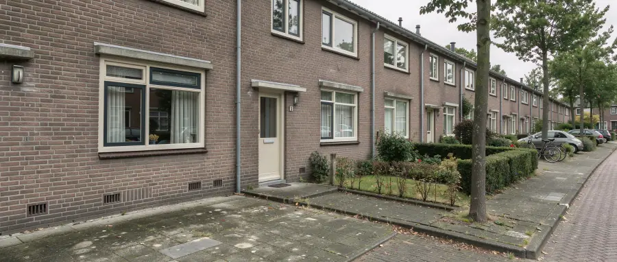 Straat met grondgebonden bakstenen woningen in een groene naoorlogse Groningse woonwijk